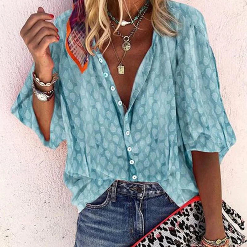 Blusa donna azzurra con motivo a pois, maniche ampie, abbinata a jeans. Accessori: collane, bracciali, pochette leopardata. Moda casual estiva.