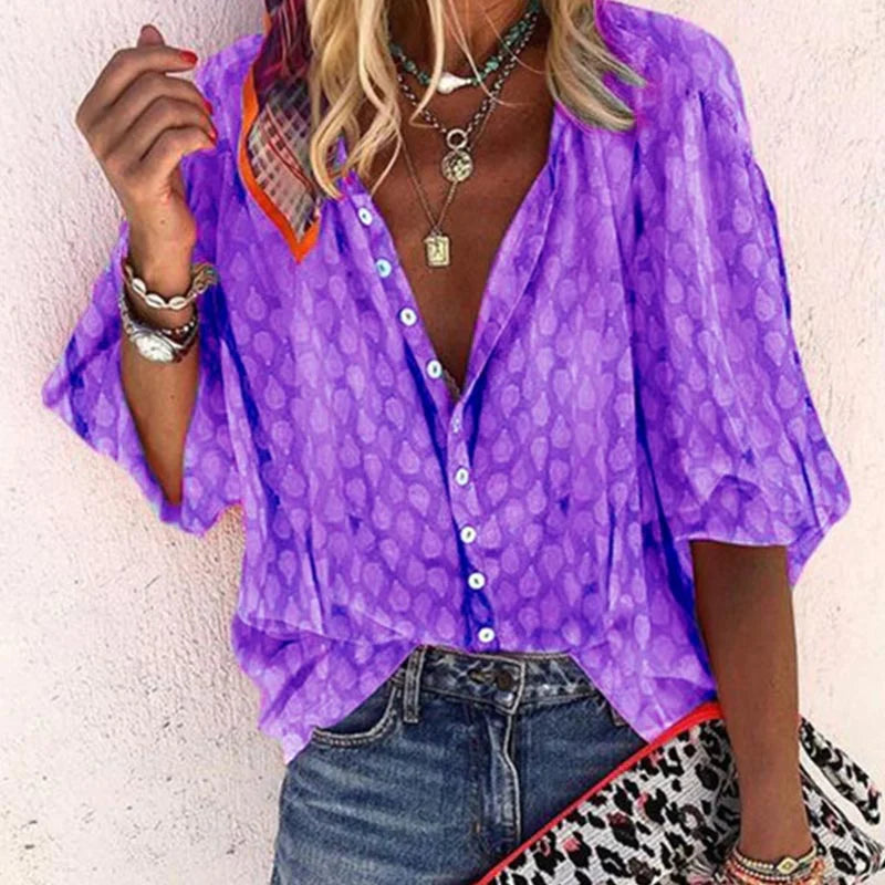 Donna con camicia viola a pois, maniche a tre quarti, abbinata a jeans. Accessori: collane e bracciali. Stile casual estivo.