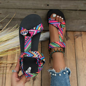 Sandali estivi da donna con cinturini colorati e suola nera, indossati su pavimento in legno. Scarpe casual perfette per la moda estiva.