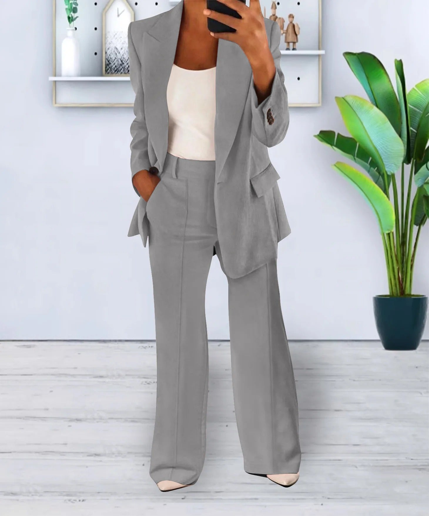 Donna in elegante completo grigio, giacca e pantaloni a zampa, davanti a pianta d'appartamento. Moda femminile, abbigliamento formale.
