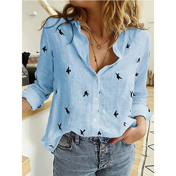Camicia azzurra da donna con stampa di uccelli neri, maniche lunghe arrotolate, abbinata a jeans. Stile casual, moda femminile, abbigliamento trendy.
