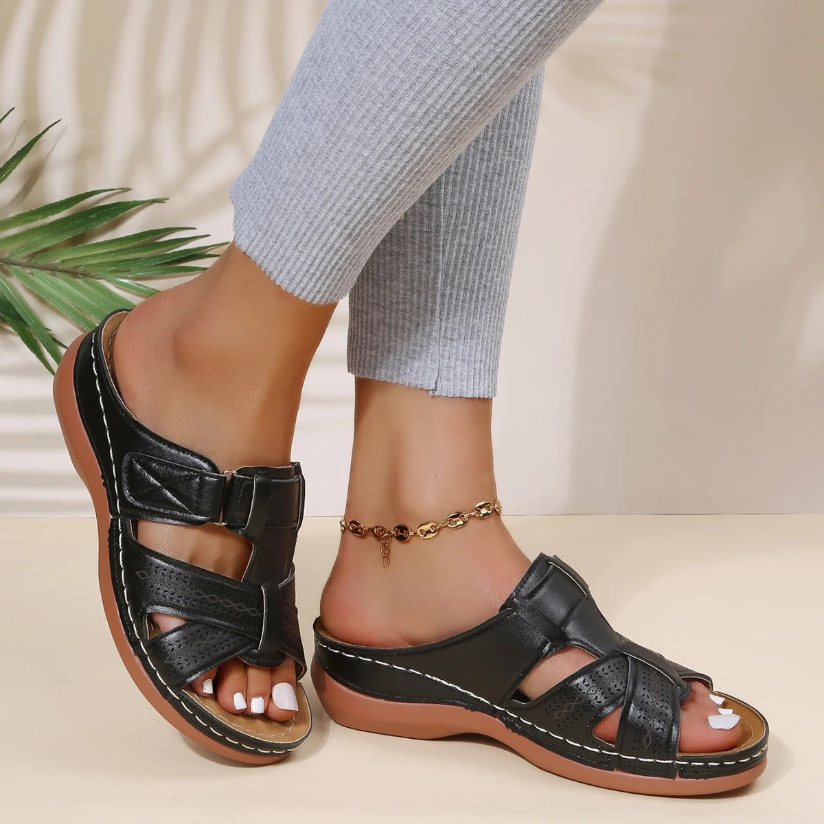 Sandali neri da donna con cinturino, suola in gomma marrone, indossati con pantaloni grigi. Design casual estivo, comodi e alla moda.
