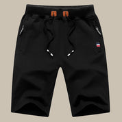 Pantaloncini sportivi neri da uomo con coulisse, tasche con zip e dettaglio bandiera. Ideali per attività sportive e tempo libero.