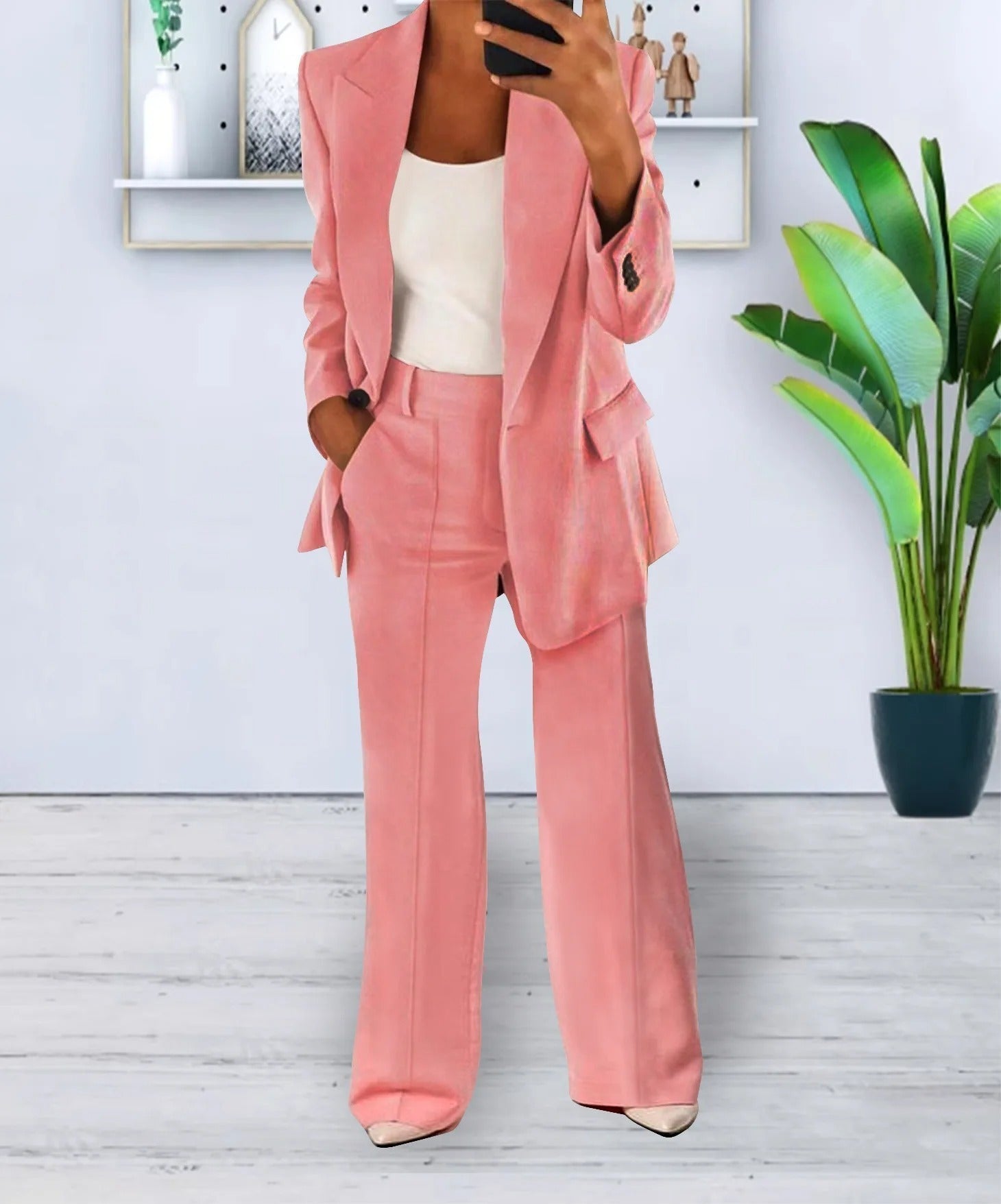 Completo donna elegante rosa, giacca e pantaloni a zampa, su sfondo moderno con pianta decorativa. Moda femminile, abbigliamento formale.
