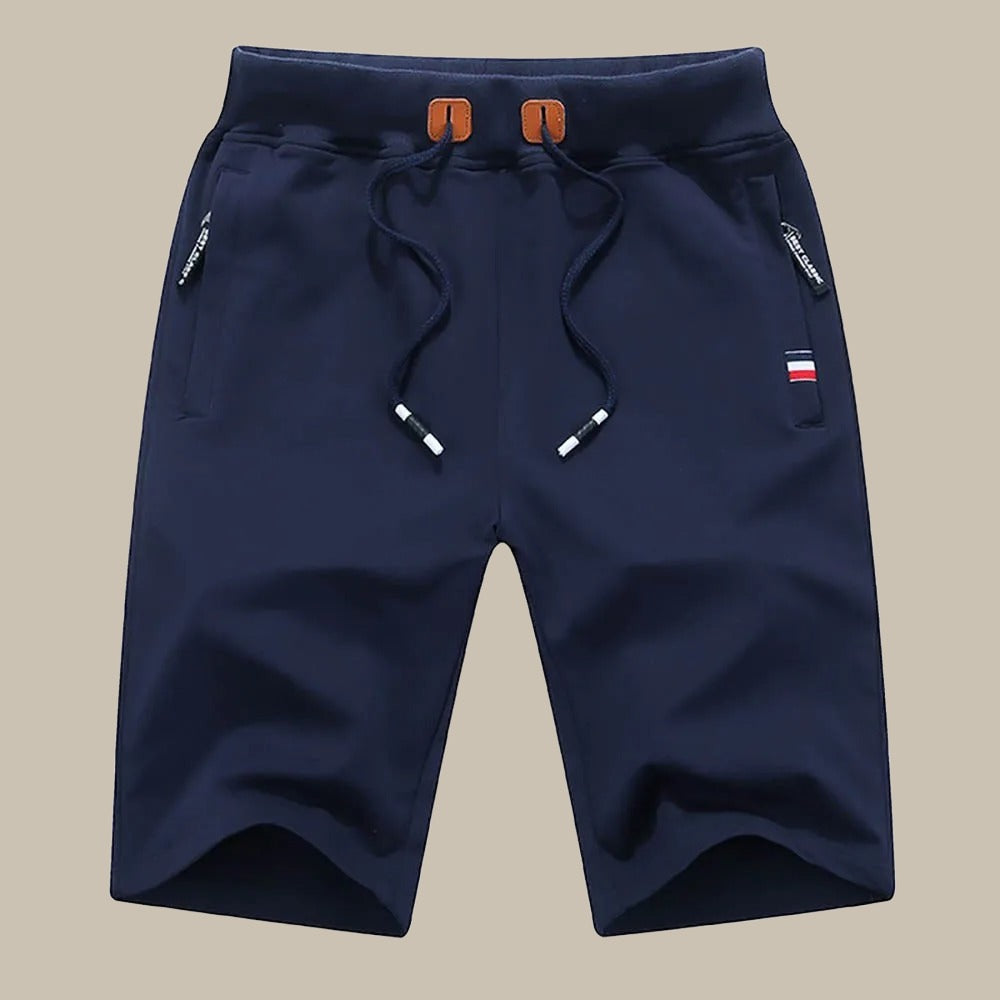 Pantaloncini sportivi blu navy da uomo con coulisse, tasche con zip e dettaglio bandiera. Ideali per attività sportive e casual.