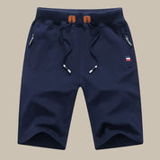 Pantaloncini sportivi blu navy da uomo con coulisse, tasche con zip e dettaglio bandiera. Ideali per attività sportive e casual.