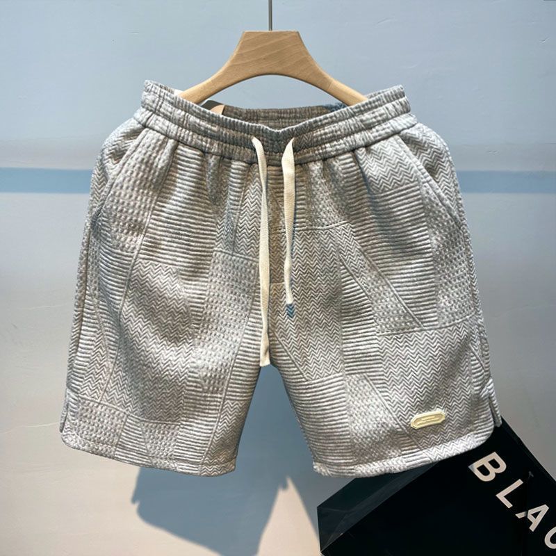 Pantaloncini grigi in tessuto lavorato a maglia, con cordoncino bianco, appesi su gruccia. Design moderno, ideale per moda casual estiva.