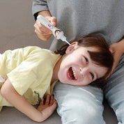 Bambino sorridente mentre un adulto utilizza un pulitore auricolare elettrico. Sicurezza, igiene orecchie, cura bambini, dispositivo pulizia.