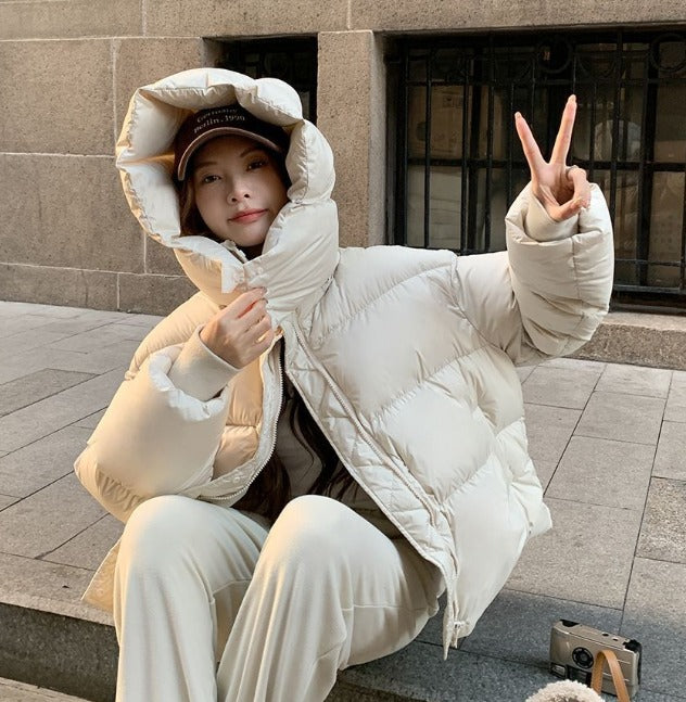 Donna con giacca piumino bianca, cappuccio e cappello beige, seduta su gradini di pietra. Moda invernale, abbigliamento caldo, stile casual.
