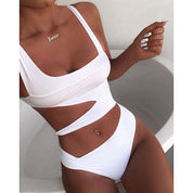 Donna in costume da bagno bianco intero con cut-out, collana dorata, unghie bianche, posa in vasca. Moda mare, abbigliamento estivo elegante.