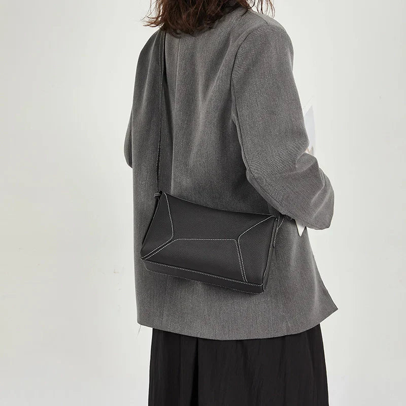 Donna con borsa a tracolla nera geometrica, giacca grigia e gonna nera. Moda elegante, accessorio femminile, stile casual chic.
