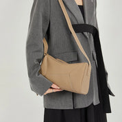 Donna con borsa a tracolla beige in pelle, indossa blazer grigio. Accessorio moda elegante, perfetto per look casual e formali.