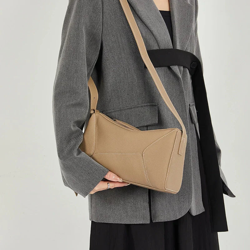 Donna con borsa a tracolla beige in pelle, indossa blazer grigio. Accessorio moda elegante, perfetto per look casual e formali.