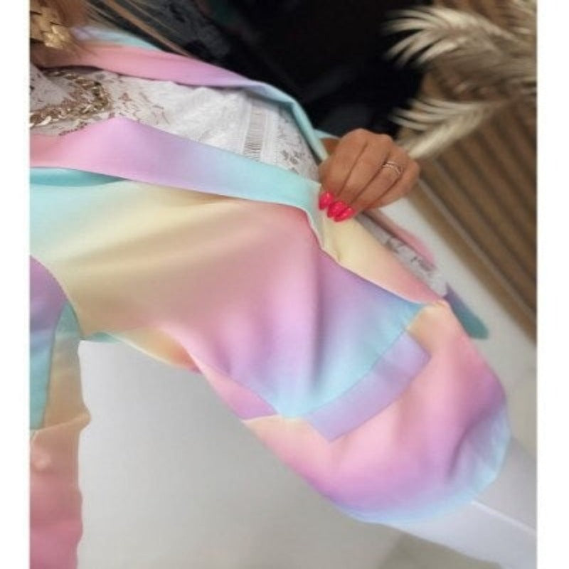 Giacca multicolore pastello sfumata, dettagliata con colori arcobaleno, indossata da una persona con unghie rosa. Moda primavera estate.