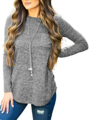 Maglia grigia a maniche lunghe da donna, abbinata a jeans strappati blu e collana lunga. Look casual e moderno per l'autunno.