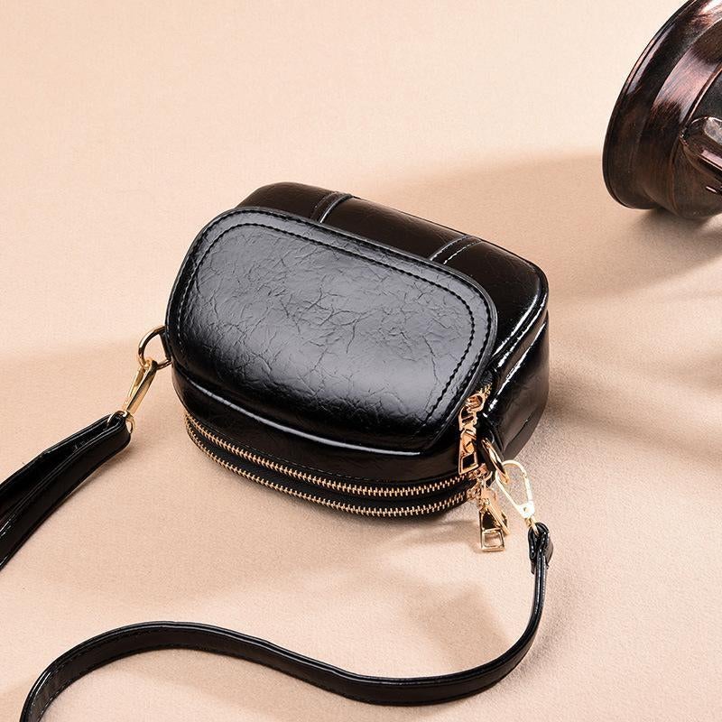 Borsa a tracolla in pelle nera lucida con cerniera dorata, design compatto e moderno, ideale per moda donna, accessori eleganti e versatili.