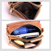 Borsa a tracolla in pelle marrone con cerniere dorate, contenente flacone blu, smartphone e accessori. Design elegante e compatto per donna.