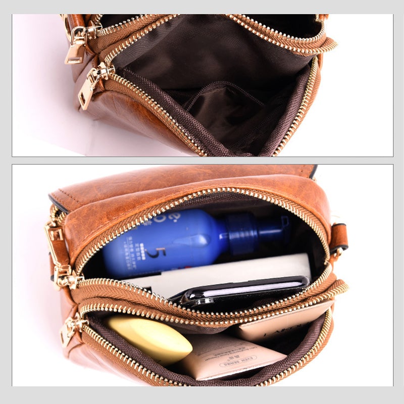 Borsa a tracolla in pelle marrone con cerniere dorate, contenente flacone blu, smartphone e accessori. Design elegante e compatto per donna.