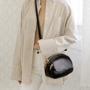 Camicia a righe beige e borsa a tracolla nera in pelle con zip dorate, moda donna elegante, accessori di tendenza, abbigliamento casual chic.