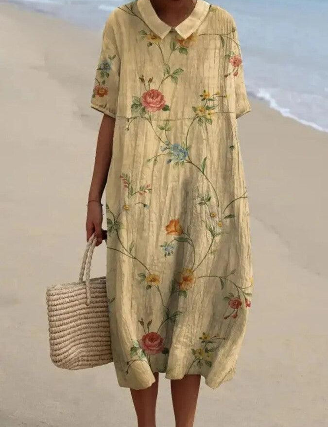 Abito estivo lungo floreale in lino, maniche corte, colletto Peter Pan, indossato su spiaggia. Borsa di paglia intrecciata. Moda donna casual.