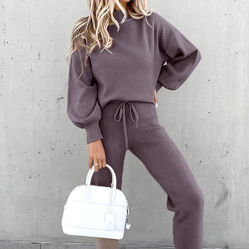 Donna in tuta grigia con borsa bianca, sfondo grigio. Moda casual, abbigliamento autunnale, stile confortevole.