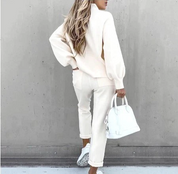 Donna di spalle con maglione bianco, pantaloni bianchi, scarpe da ginnastica e borsa bianca. Moda casual elegante, look monocromatico.