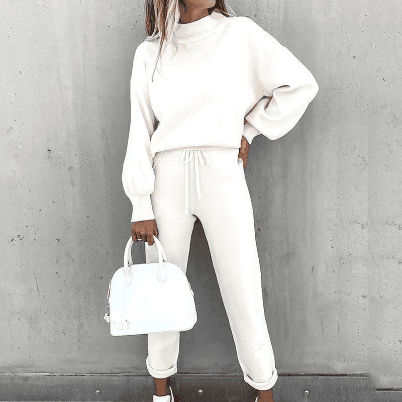 Donna con completo bianco casual, maglione e pantaloni, borsa a mano bianca, sfondo grigio. Moda donna, abbigliamento elegante, stile minimalista.